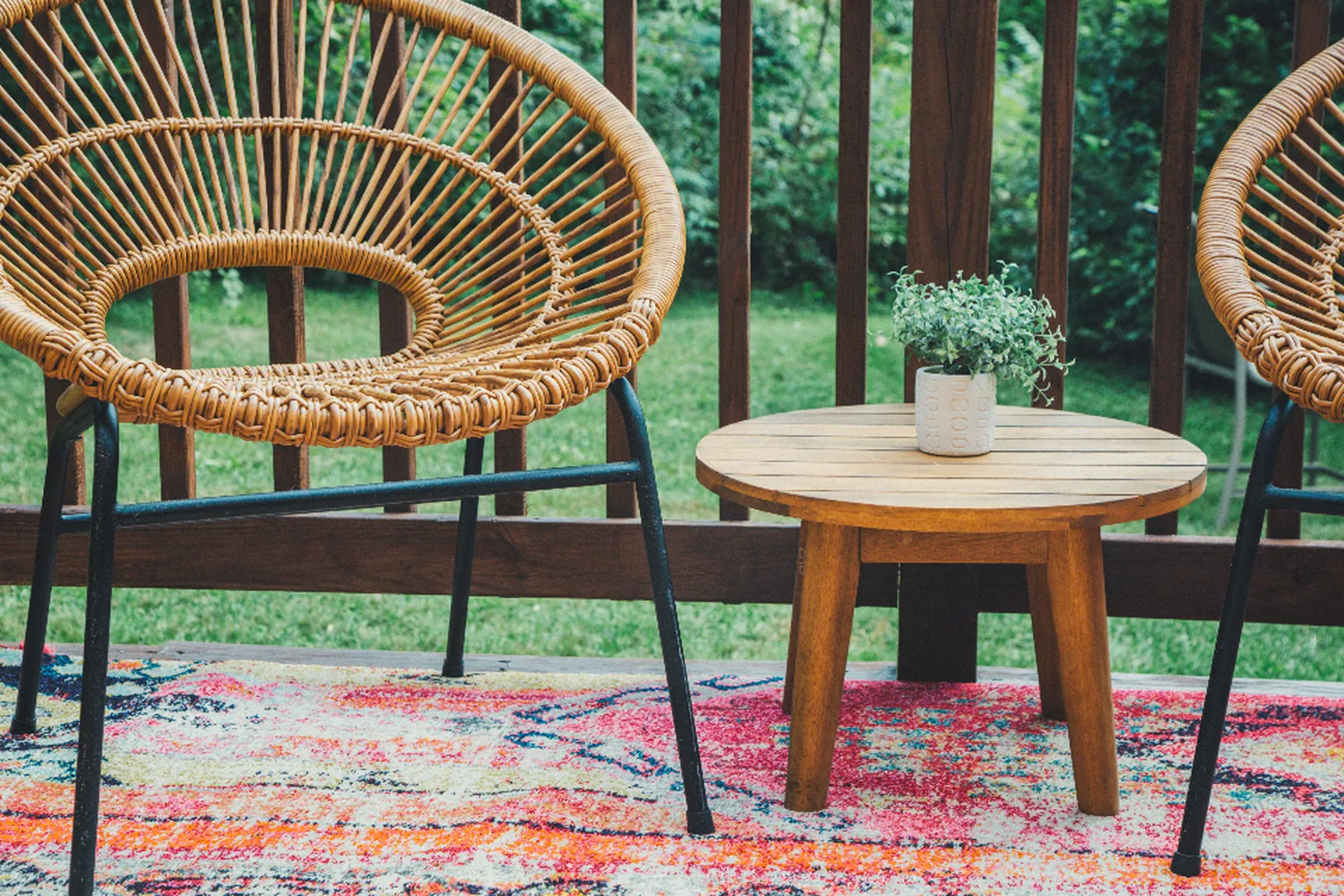 Rattan chairs and a low table on a wood deck behind a timber railing