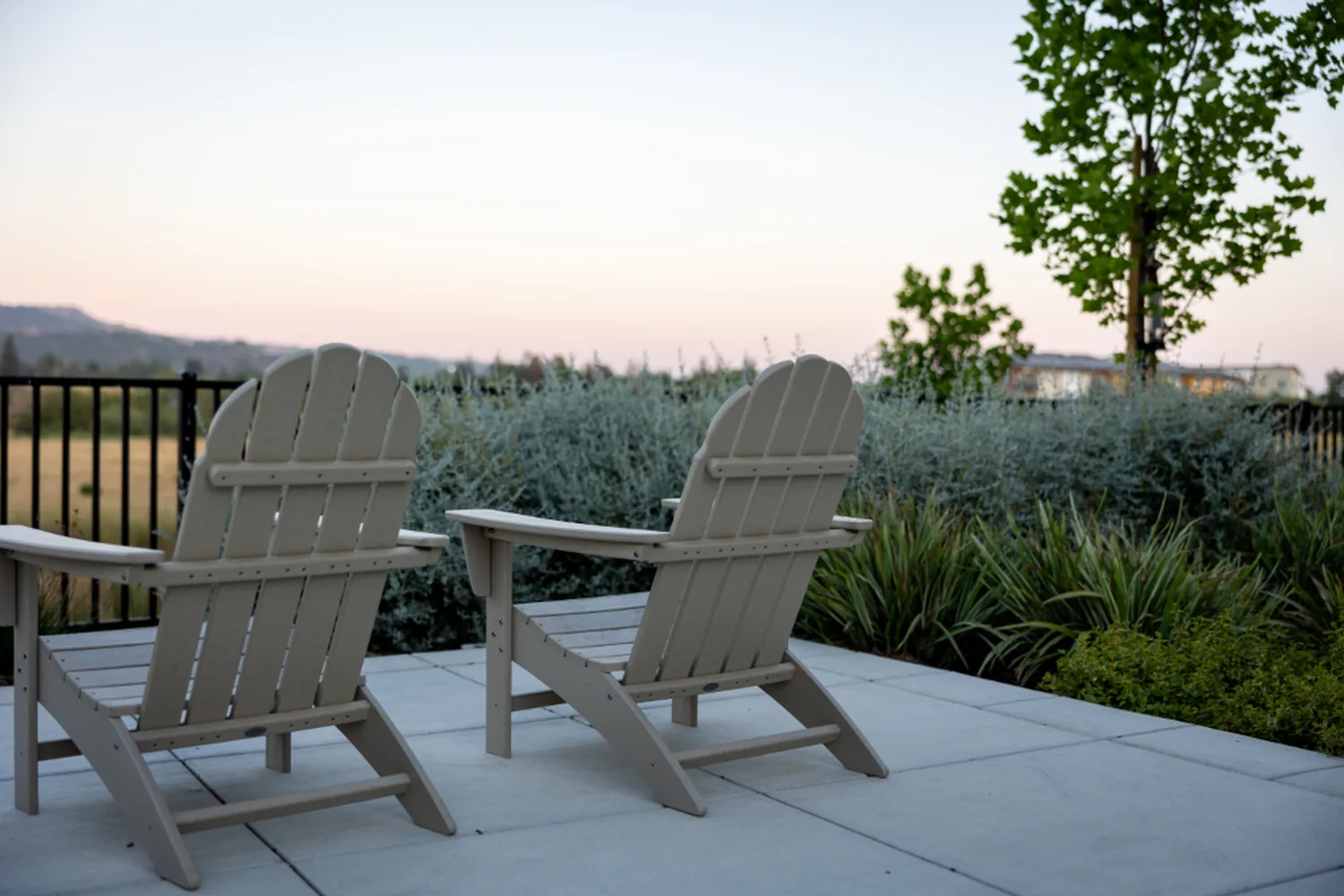 Two Adirondack chairs on a bare concrete patio with a metal rail