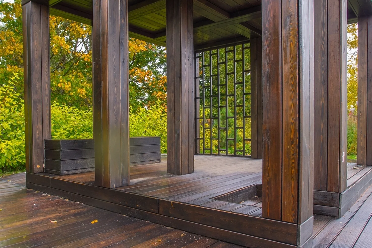 Dark-stained covered deck with heavy square posts and a slatted screen panel