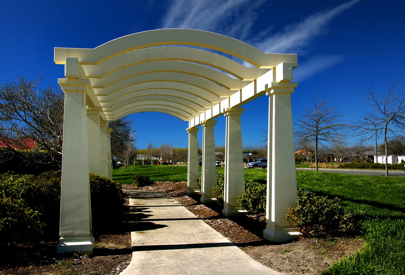 White pergola with arched beams over a garden walkway