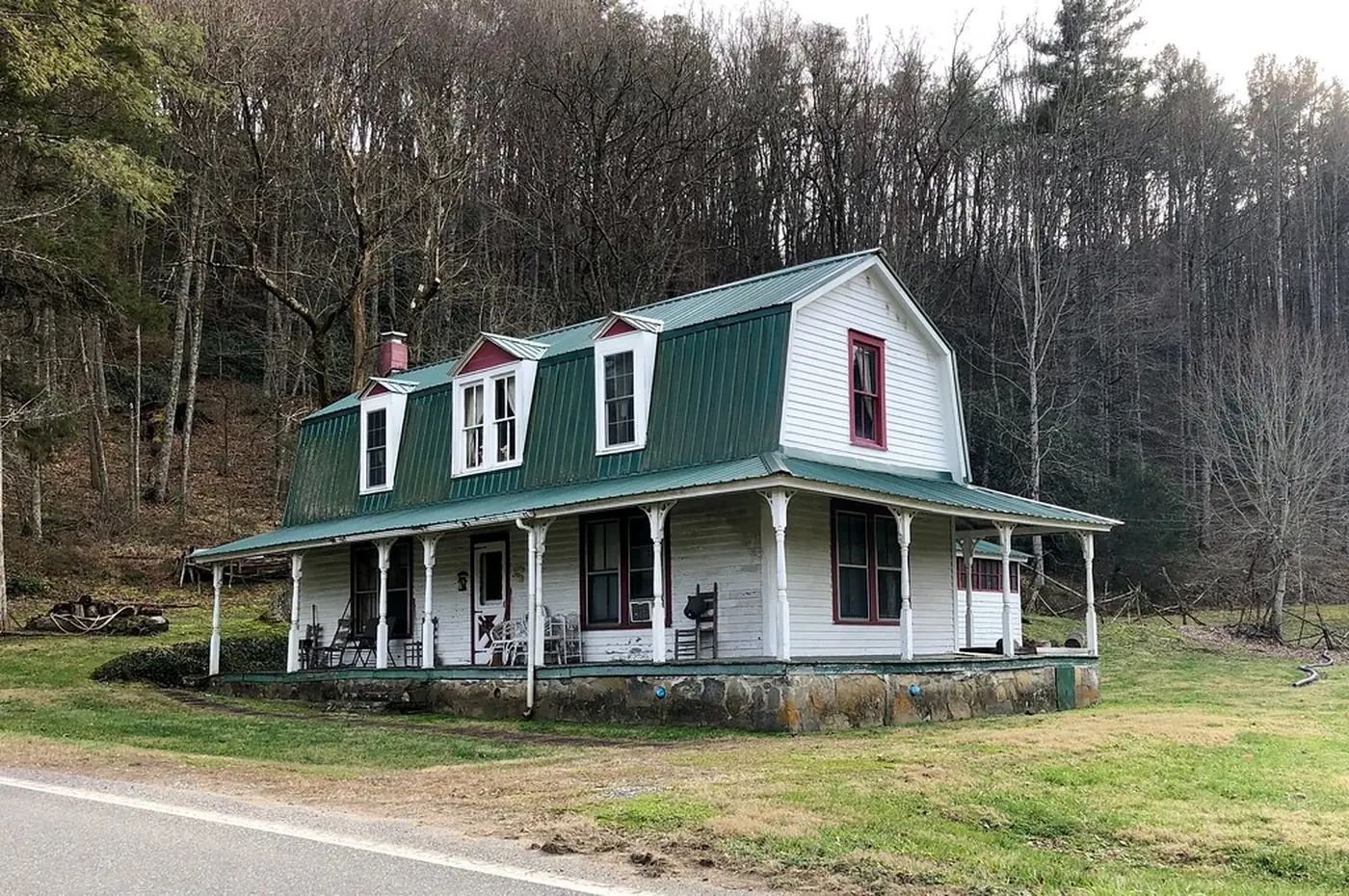 White farmhouse with a wraparound covered porch and turned posts